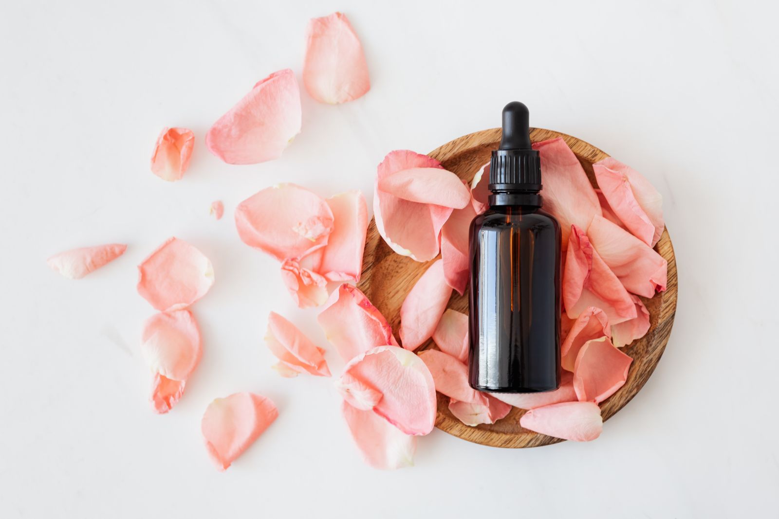 Unbranded amber dropper bottle with rose petals on marble — Du Joli beauty editorial