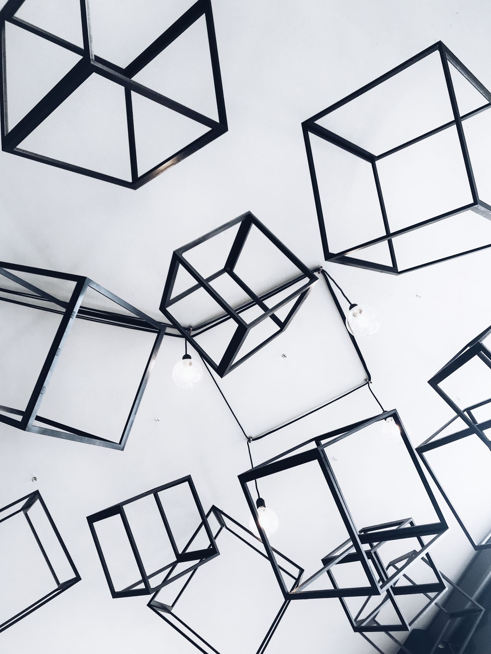 Minimal black geometric wireframe cubes on bright white studio — daylight editorial, no neon