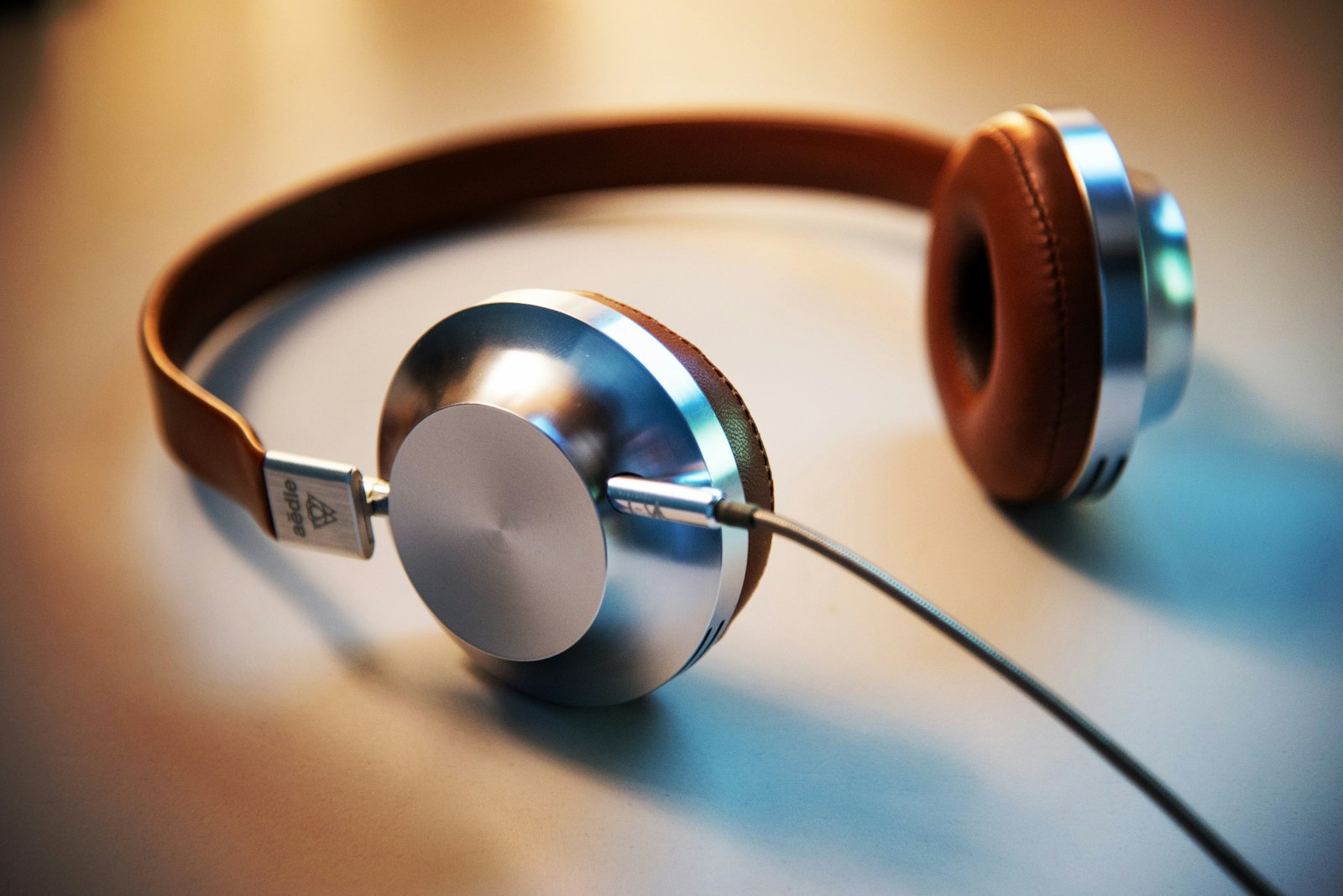 Brushed metal headphones on desk in soft daylight — minimal metal desk object editorial, no neon