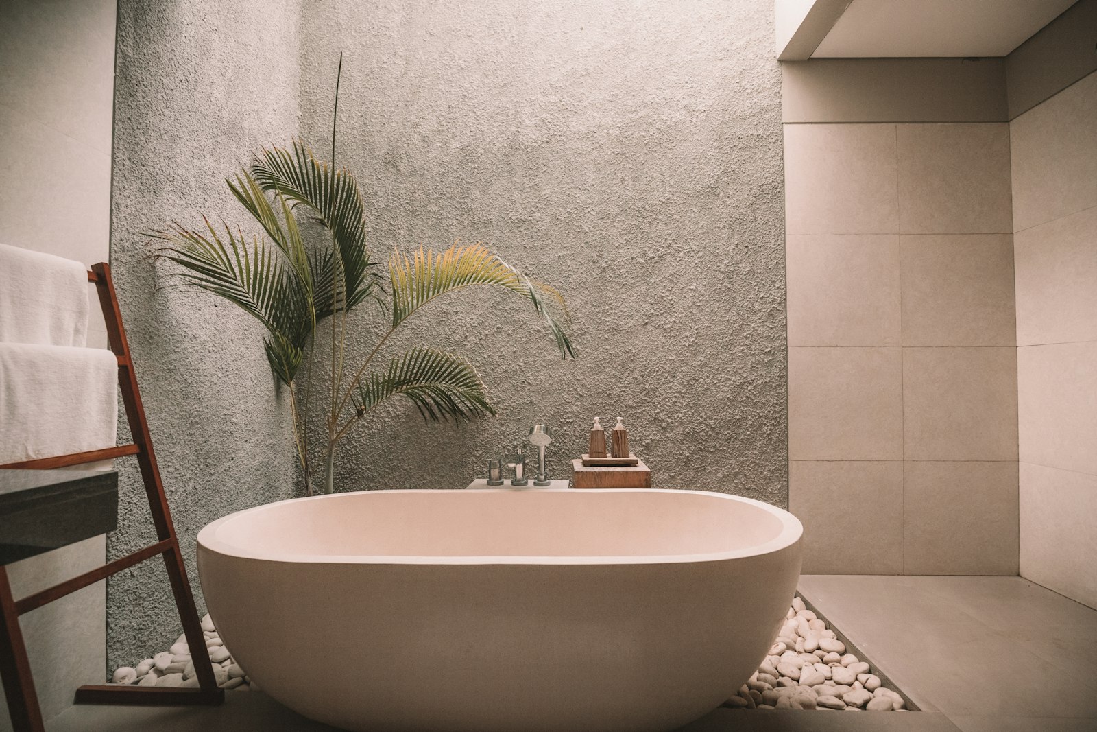 Freestanding spa bathtub with pebbles, towels, and soft daylight — wellness ritual interior