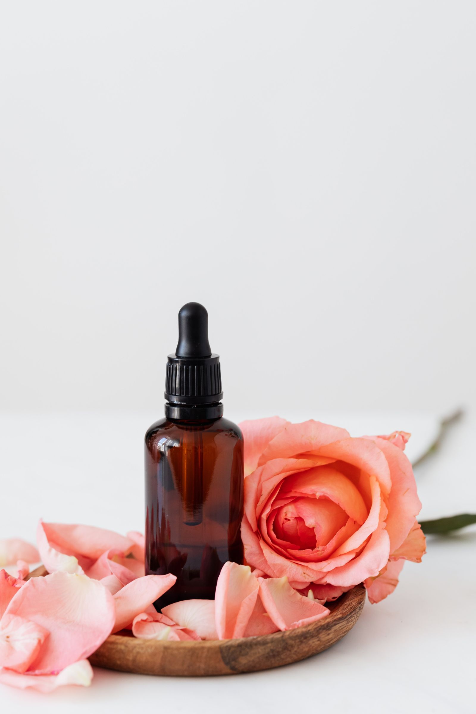Unbranded amber dropper bottle with peach rose on wooden tray — product still-life studio