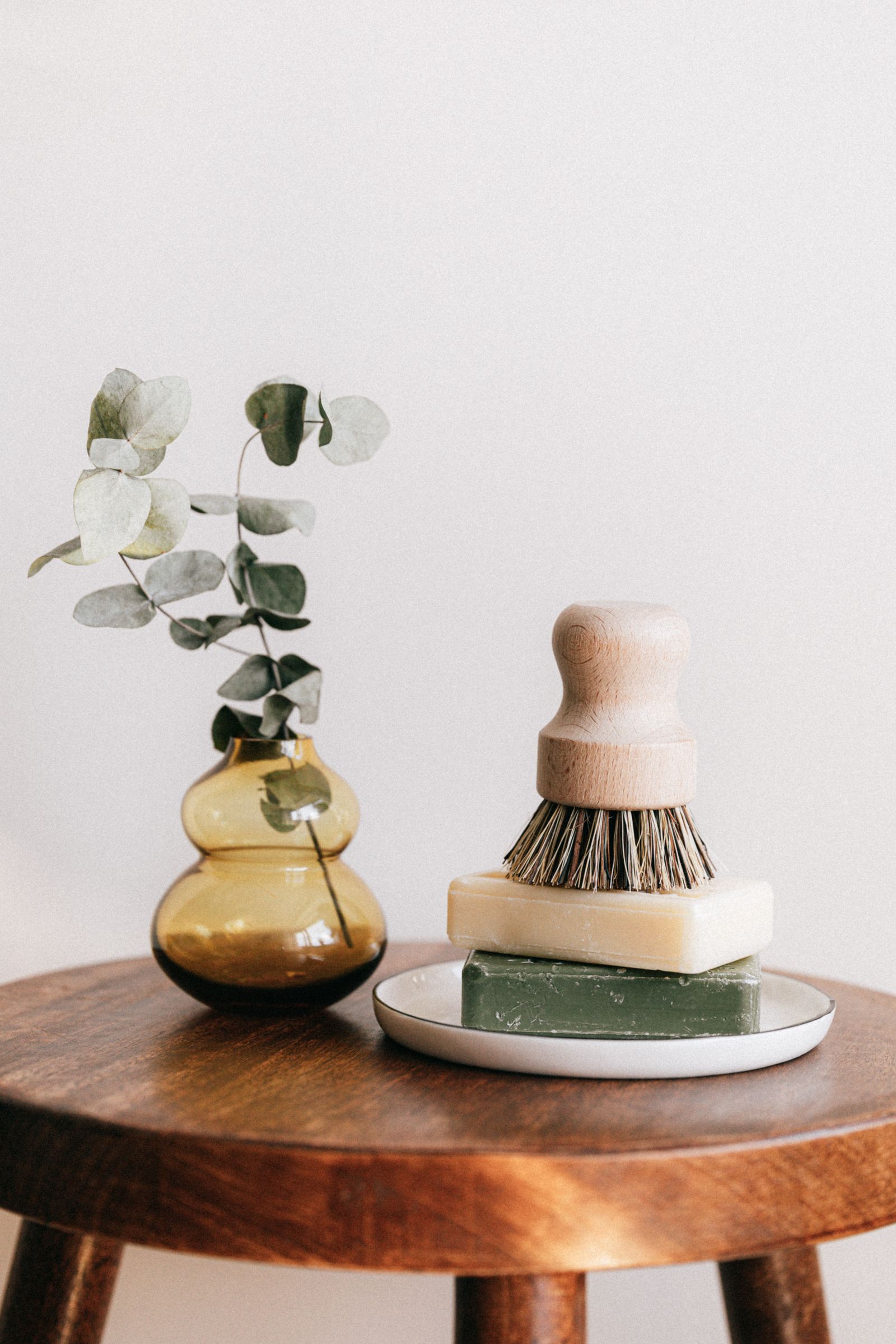 Unbranded artisanal soaps, wood brush, and eucalyptus on wooden stool — soft beauty daylight