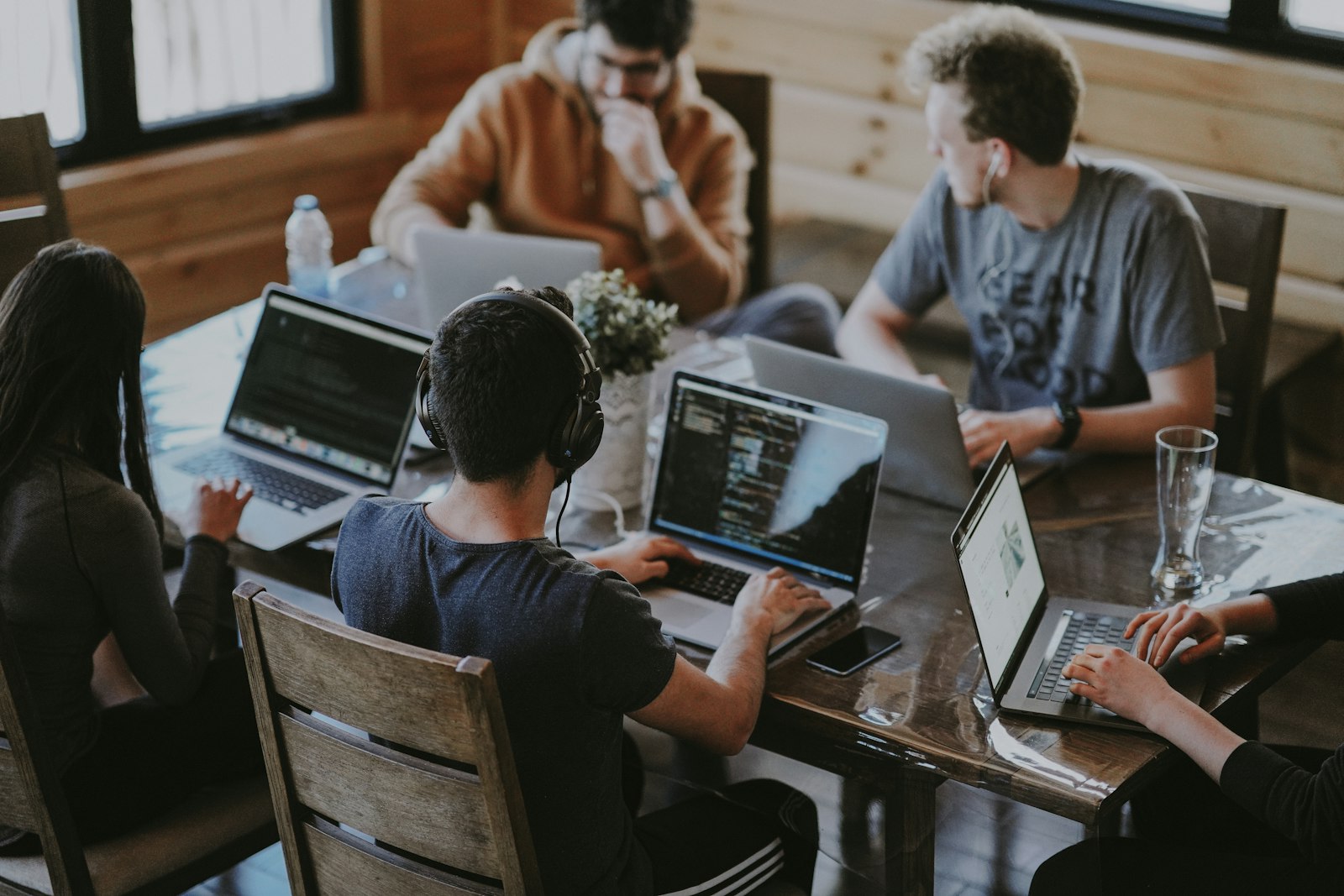 Creative collective team collaborating around loft workspace table with laptops — daylight